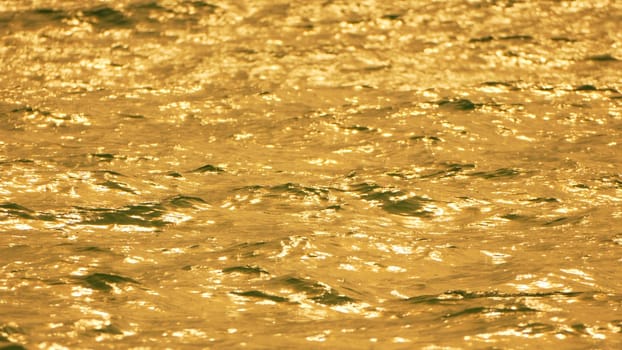 Close-up of golden, rippling water reflecting sunlight. The surface is textured and shimmering, creating a dynamic visual.