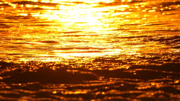 A close-up shot of molten metal, glowing intensely with a fiery orange hue. The surface is rippling and bubbling, indicating extreme heat.