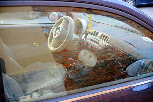Cremona, Itally - October 6th 2024 Interior of a dusty fiat 500 lounge with beige decor, showcasing steering wheel, dashboard, gear stick, and seats against a weathered brick wall