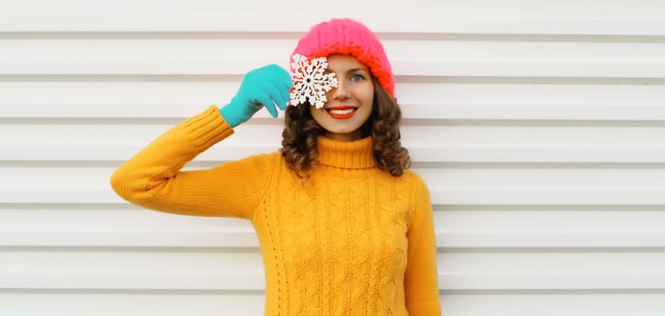 Winter christmas portrait of happy smiling young woman with snowflakes decoration toys having fun wearing yellow sweater, pink hat on white background