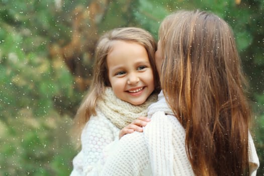 Portrait of happy joyful mother and little girl child together laughing near Christmas tree in forest