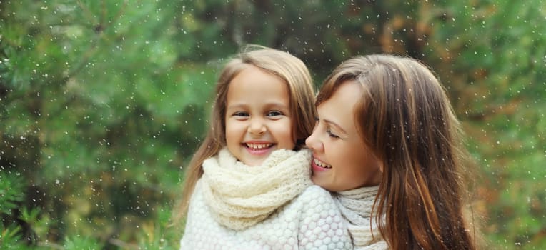 Portrait of happy joyful mother and little girl child together laughing near Christmas tree in forest