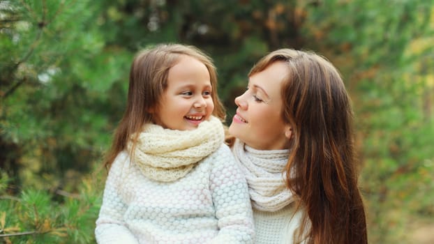 Portrait of happy joyful mother and little girl child together laughing near Christmas tree in forest