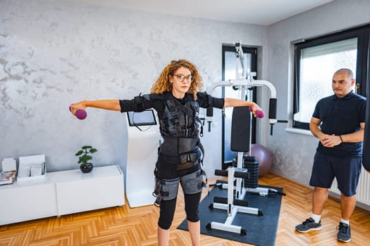 A person engages in an EMS workout while holding weights.