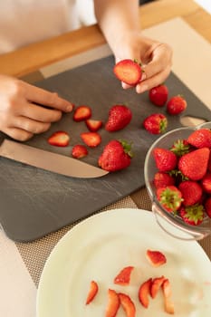 a woman's hands cut strawberries into slices.