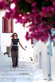 Young woman in black dress walking on a street on the Greek islands among bougainvillea