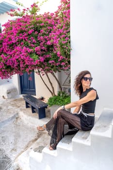 Young woman in black dress sitting on a street on the Greek islands among bougainvillea