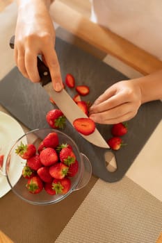 women's hands slicing strawberries on a board with a knife.