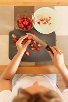 a woman's hands cut strawberries into slices.