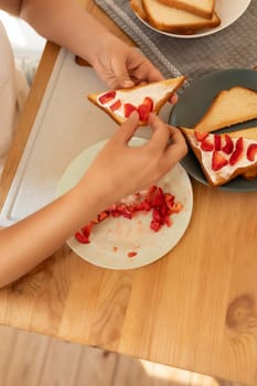 women's hands make a homemade strawberry sandwich.