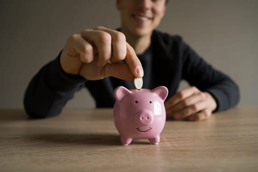 A young man is sitting at his workplace, in the foreground is a piggy bank. A businessman saves his money, takes care of the safety of his earnings, develops his business and makes investments.