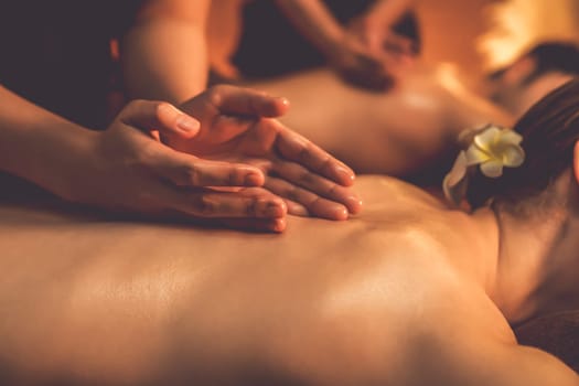 Closeup couple customer enjoying relaxing anti-stress spa massage and pampering with beauty skin recreation leisure in warm candle lighting ambient salon spa at luxury resort or hotel. Quiescent