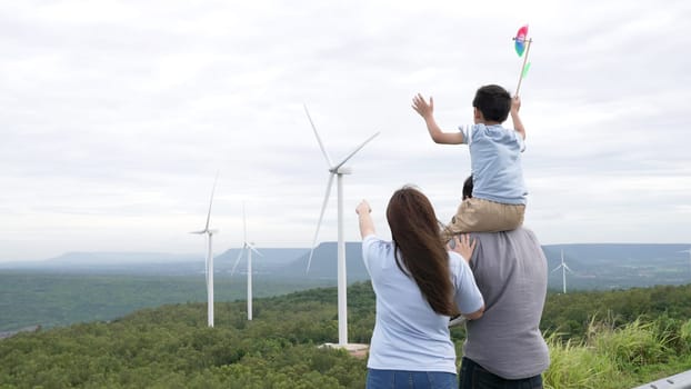 Concept of progressive happy family enjoying their time at the wind turbine farm. Electric generator from wind by wind turbine generator on the country side with hill and mountain on the horizon.