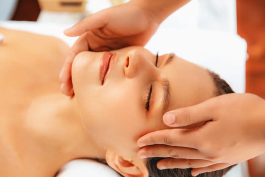 Closeup woman enjoying relaxing anti-stress head massage and pampering facial beauty skin recreation leisure in dayspa modern light ambient at luxury resort or hotel spa salon. Quiescent