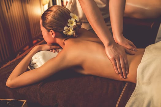 Caucasian couple customer enjoying relaxing anti-stress spa massage and pampering with beauty skin recreation leisure in warm candle lighting ambient salon spa at luxury resort or hotel. Quiescent