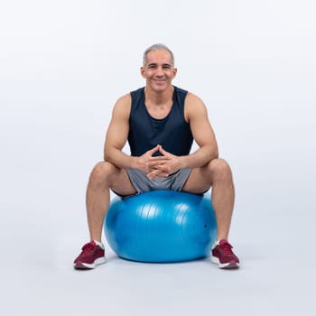 Full body length shot athletic and sporty senior man with fitness exercising ball in sitting posture on isolated background. Healthy active and body care lifestyle after retirement. Clout