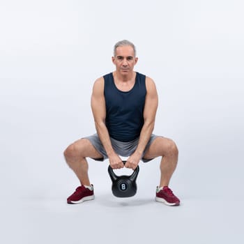 Full body length shot athletic and sporty senior man doing squat with kettlebell for body workout on isolated background. Healthy active physique and body care lifestyle after retirement. Clout