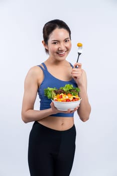 Young sporty Asian woman in sportswear holding salad bowl fill with vibrant of fruit and vegetable. Natural youthful and fit body lifestyle with balance nutrition on isolated background. Vigorous