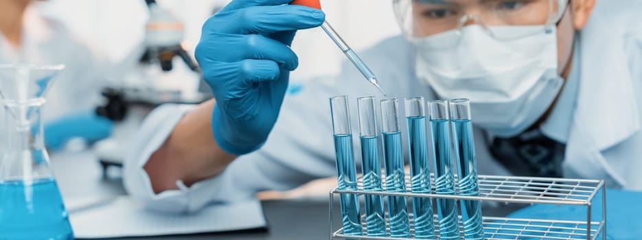 Group of dedicated scientist conduct chemical experiment in medical laboratory, carefully drop precise amount of liquid from pipette into test tube for vaccine drug or antibiotic development. Neoteric