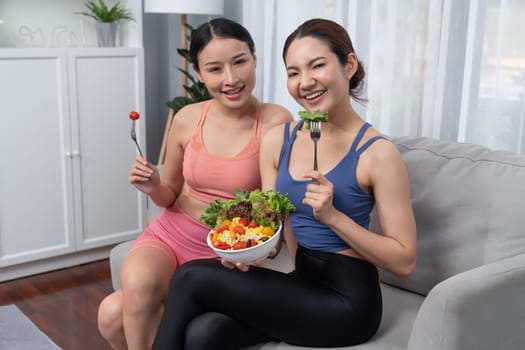 Young sporty Asian women in sportswear holding salad bowl together fill with vibrant of fruit and vegetable. Natural youthful and fit body lifestyle with balance nutrition and home exercise. Vigorous