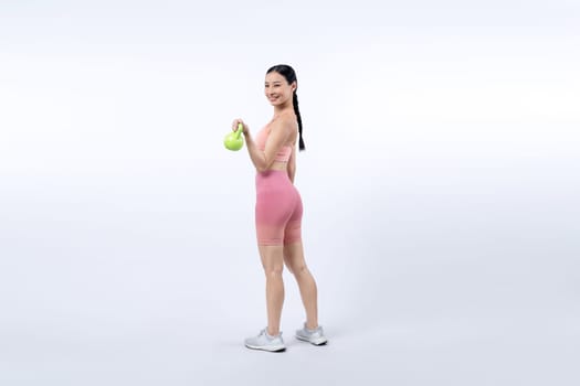 Vigorous energetic woman doing kettlebell weight lifting exercise on isolated background. Young athletic asian woman strength and endurance training session as body workout routine.