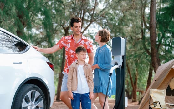 Outdoor adventure and family vacation camping in nature travel by eco friendly car for sustainable future. Lovely family recharge EV car with EV charging station in campsite. Perpetual