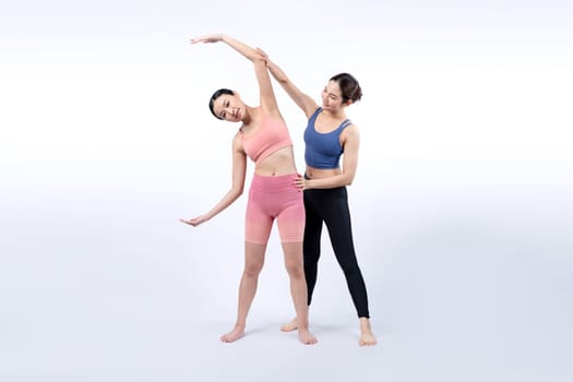 Asian woman in sportswear doing yoga exercise in standing pose with her trainer or yoga buddy. Healthy body care and meditation yoga lifestyle in full shot on isolated background. Vigorous