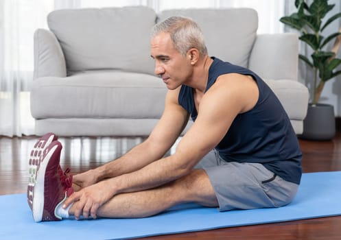 Active and fit senior man warmup and stretching before home exercising routine at living room. Healthy fitness lifestyle concept after retirement for pensioner. Clout