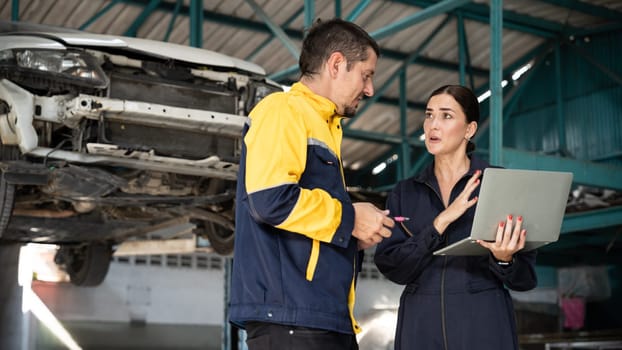 Two vehicle mechanic working together, conduct car inspection with laptop. Automotive service technician in uniform carefully make diagnostic troubleshooting to identify error. oxus