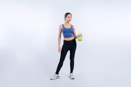 Vigorous energetic woman doing kettlebell weight lifting exercise on isolated background. Young athletic asian woman strength and endurance training session as body workout routine.