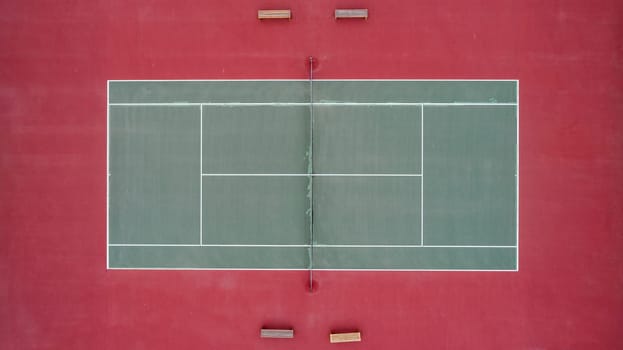 A tennis court with a net and two benches. The court is red and green