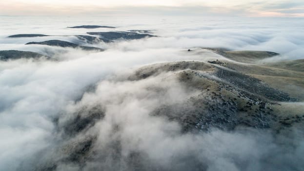 The sky is covered in a thick layer of fog, creating a moody and mysterious atmosphere. The fog is so dense that it obscures the landscape below, making it difficult to discern any specific details