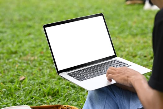 Close up of man using laptop in city park on green grass.