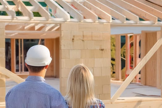 ai generated,A couple stands in front of their partially built house, observing the progress. The man wears a hard hat, suggesting involvement in the construction process and ensuring safety.