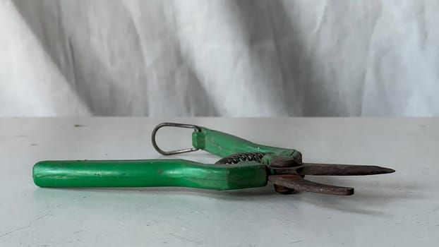 Old green scissors rest on a white table, showing wear in a bright setting.
