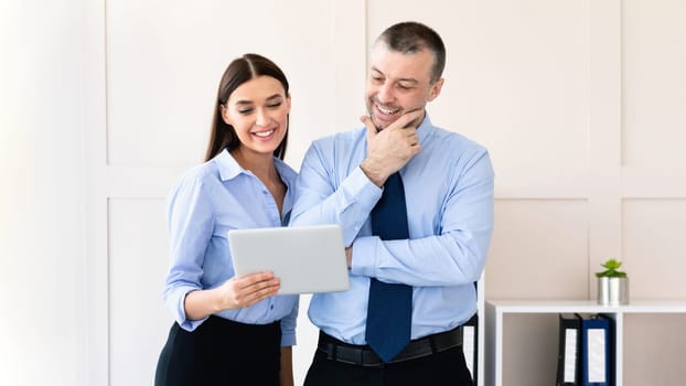 Businesswoman Showing Digital Tablet To Coworker Man Standing In Modern Office. Corporate Communication