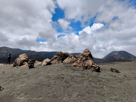 A breathtaking view of Mount Bromo, Indonesia. The volcano's peak is shrouded in dramatic clouds, creating a sense of awe and mystery. The foreground features a rocky landscape