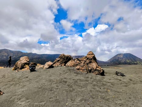 A breathtaking view of Mount Bromo, Indonesia. The volcano's peak is shrouded in dramatic clouds, creating a sense of awe and mystery. The foreground features a rocky landscape