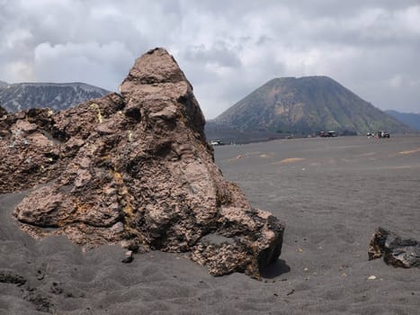 A breathtaking view of Mount Bromo, Indonesia. The volcano's peak is shrouded in dramatic clouds, creating a sense of awe and mystery. The foreground features a rocky landscape