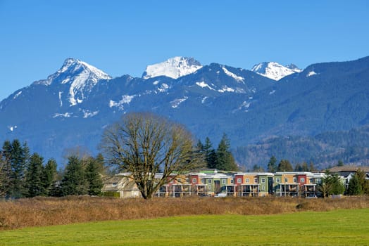 New residential townhouses on blue sky and mountain background. Winter season in Fraser valley, British Columbia.