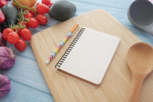 A notebook and colorful pen next to fresh vegetables on a wooden cutting board, ready for cooking