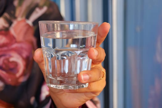 A clear and pristine glass of water is held in a hand, set against a vibrant background