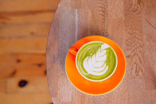 A vibrant matcha latte with intricate leaf art, sitting on a rustic wooden table