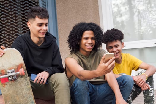 three happy multiethnic teen friends sharing mobile phone sitting together with on street, concept of youth and technology of communication