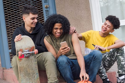 three happy multiethnic teen friends having fun sharing mobile phone sitting together with on street, concept of youth and technology of communication