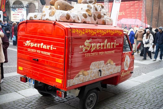Cremona, Italy - November 15th 2024 Small red piaggio ape car with sperlari nougat advertisement parked on a cobblestone street in italy
