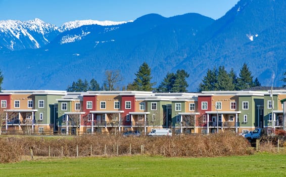 New residential townhouses on blue sky and mountain background. Winter season in Fraser valley, British Columbia.