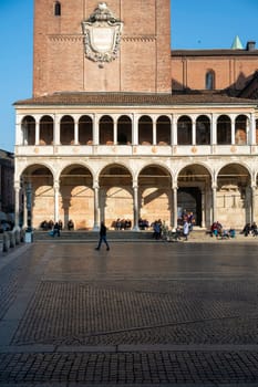 Cremona, Italy - November 20th 2024 Tourists sitting and walking in piazza grande in front of the ghirlandina tower and palazzo comunale in modena, italy, on a sunny winter day