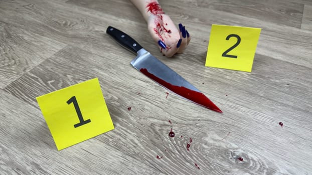 Evidence markers near crime scene of murder of girl next to murder weapon. Bloody marks on knife and hand of girl on floor of apartment. Marking evidence at bloody crime scene with knife