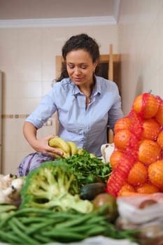 A woman sorting and arranging fresh fruits and vegetables in the kitchen. She appears relaxed and focused, emphasizing healthy lifestyle and natural food choices.